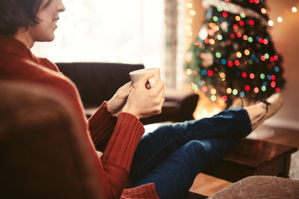 Woman sitting relaxed in front of Christmas tree praticing holiday self-care.