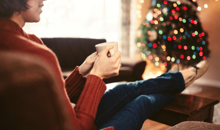 Woman sitting relaxed in front of Christmas tree praticing holiday self-care.