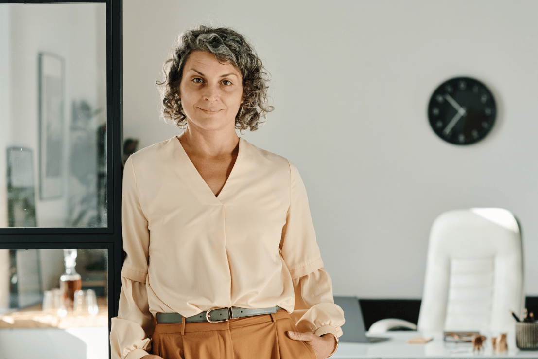 Serious looking woman dressed in business casual attired standing in corporate office.