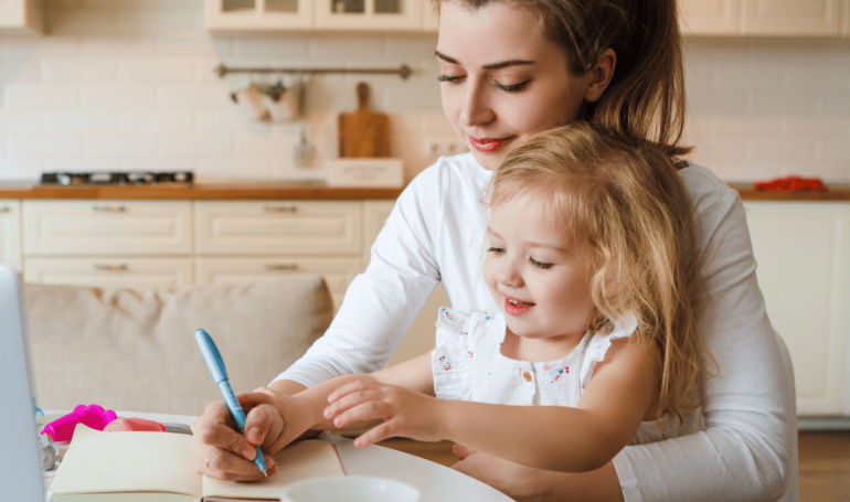 Women sitting in kitchen with child writing notes.