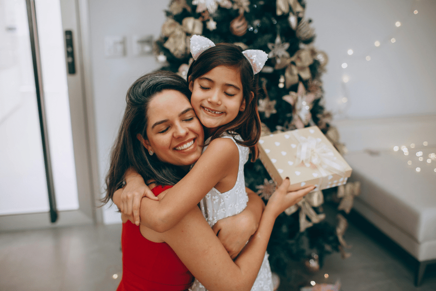 Mother and young daughter hugging and smiling in front of christmas tree.