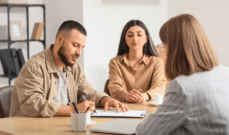 Couple getting divorce sitting with mediator at table signing papers